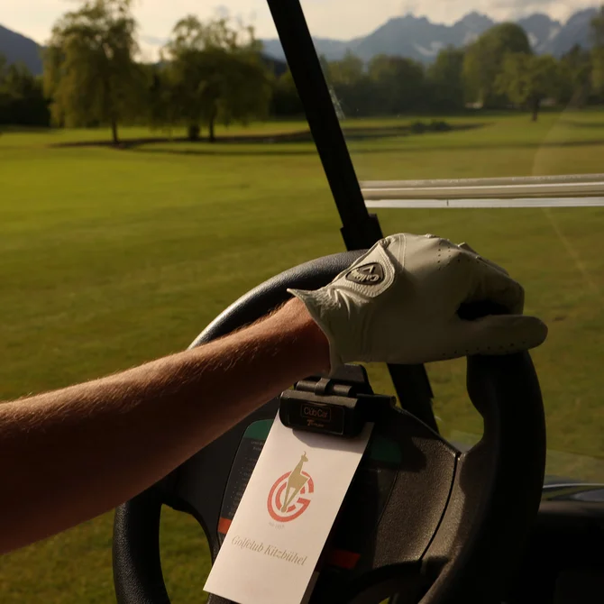 Arm with golf glove on steering wheel of golf cart on golf course
