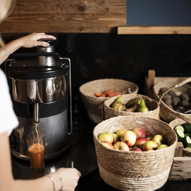 Person presst frischen Saft mit Entsafter, Körbe mit Obst und Gemüse