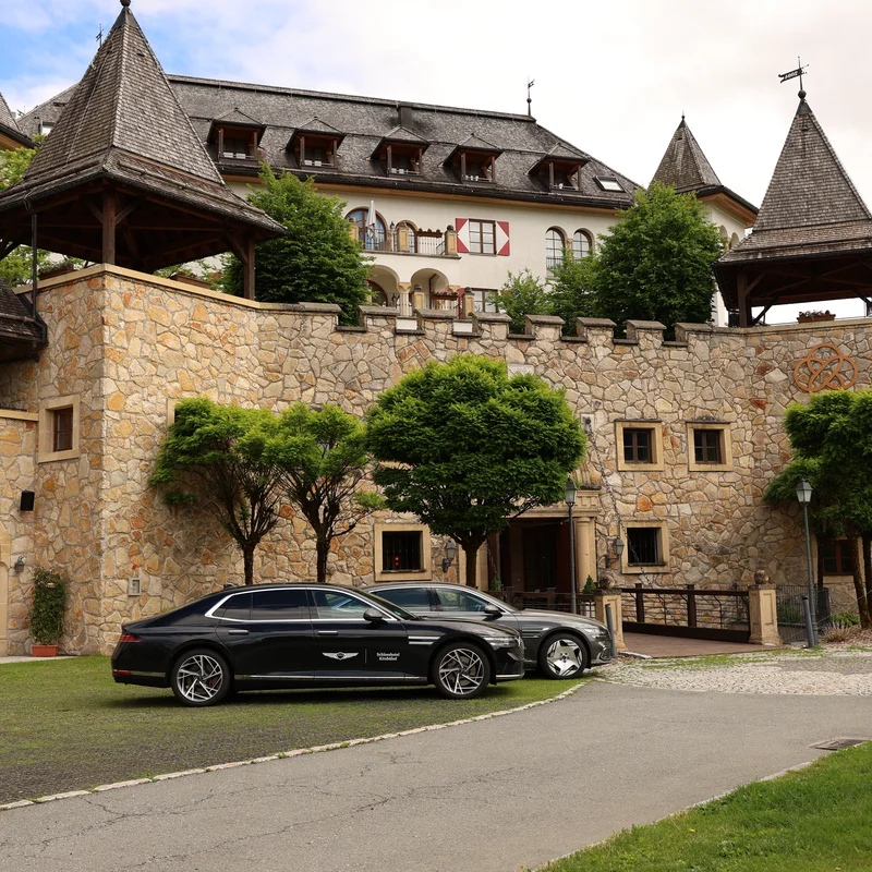Steinernes Schloss mit Türmen und zwei schwarzen Autos davor