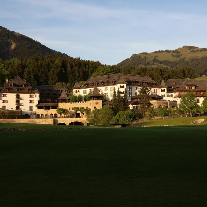 Large hotel building in front of forested mountains at sunset