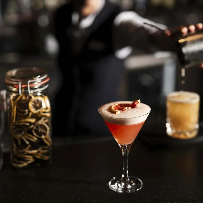 Ein Barkeeper gießt einen Cocktail mit Zitrus-Trockengarnitur vor zwei Gläsern