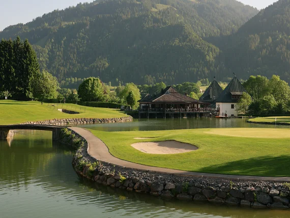 Golfplatz am See mit Bergkulisse und Clubhaus bei sonnigem Wetter