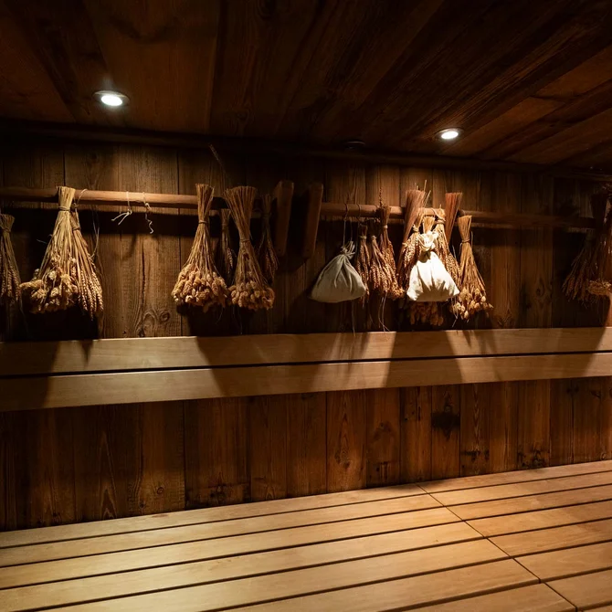 Rustikaler Saunaraum mit hölzernen Bänken und aufgehängten Kräuterbündeln